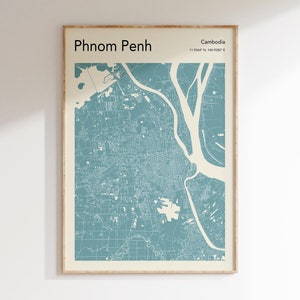 May include: A blue and white map print of Phnom Penh, Cambodia. The map shows the city's streets and waterways. The title "Phnom Penh" and the coordinates "11.5564° N, 104.9302° E" are printed at the top of the map.