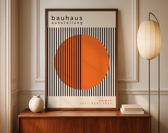 May include: A framed Bauhaus exhibition poster with a geometric design. The poster features a large orange circle bisected by vertical black lines against a cream background. The text "bauhaus ausstellung" is at the top, with "WEIMAR JULI-SEPT 1923" at the bottom.