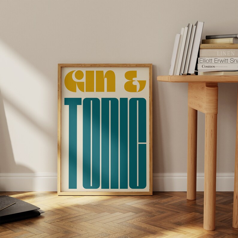 May include: A framed print with the text "Gin & Tonic" in a retro style font. The text is in yellow and teal on a white background.