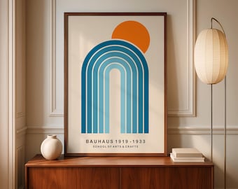 May include: A framed Bauhaus art print with a blue arch and orange sun on a cream background. The text reads "BAUHAUS 1919-1933 SCHOOL OF ARTS & CRAFTS". The print is displayed on a wooden cabinet. The print is in a brown frame.