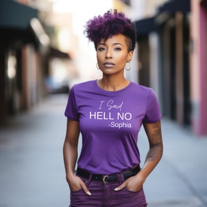Pode incluir: Uma mulher vestindo uma camiseta roxa com o texto "I Said HELL NO -Sophia" impresso nela. Ela está em pé em um ambiente urbano.