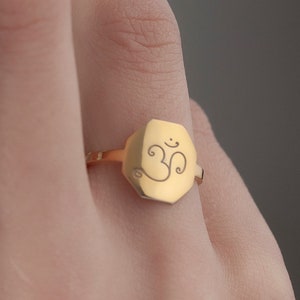 May include: A gold ring with a hexagonal shaped top featuring the Om symbol engraved on it.