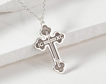 May include: A silver chain necklace with a silver cross pendant. The cross has a detailed design and the inscription "IC XC" on it.