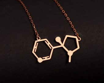 May include: A rose gold necklace with a pendant shaped like a chemical structure. The pendant is made of metal and has a shiny finish.