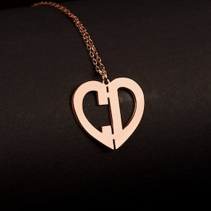 May include: A rose gold necklace with a heart-shaped pendant featuring the letters "C" and "D" intertwined. The pendant is on a delicate chain.