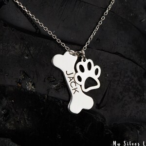 May include: Silver necklace with a bone charm engraved with the name "JACK" and a paw print charm.
