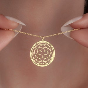 May include: A gold necklace with a circular pendant featuring a geometric design. The pendant is made of thin metal and has a delicate, intricate pattern.