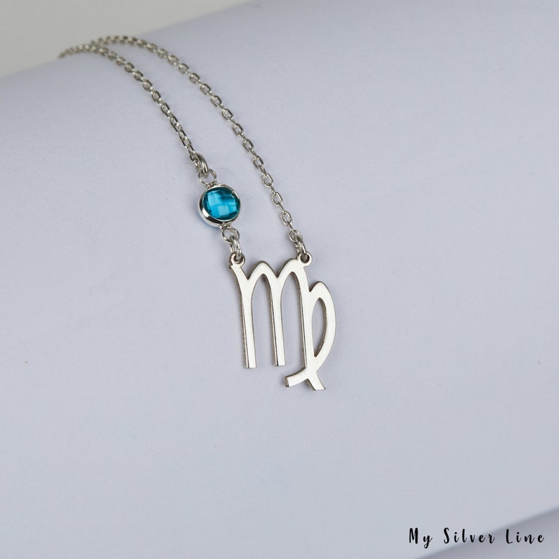 May include: Silver necklace with a Virgo zodiac symbol charm and a blue gemstone. The necklace is on a white background.