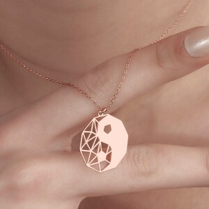 May include: A rose gold necklace with a geometric yin yang pendant.