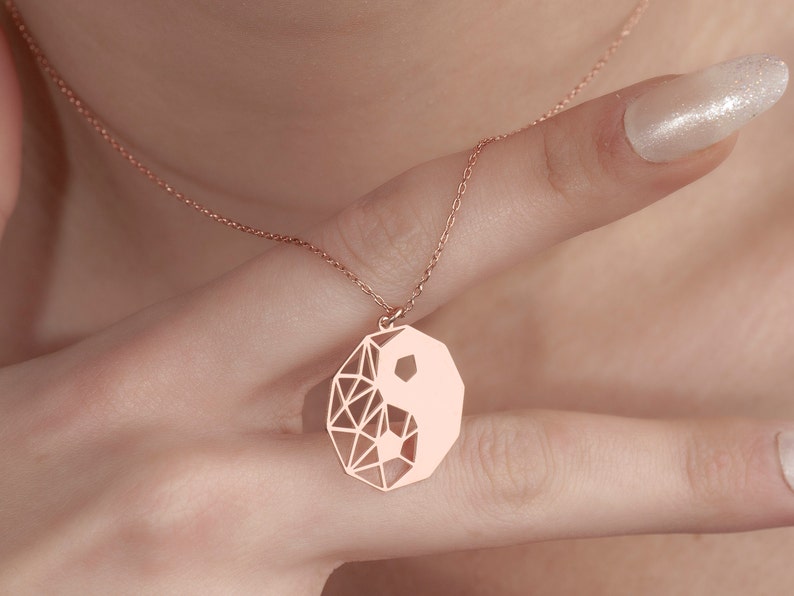 May include: A rose gold necklace with a geometric yin yang pendant.