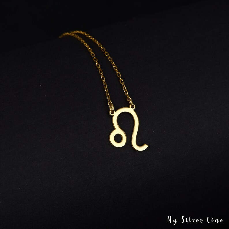 May include: Gold chain necklace with a Leo zodiac sign pendant. The pendant is a simple outline of the Leo constellation.