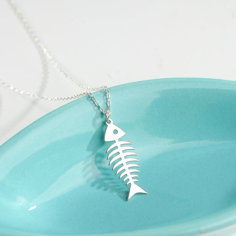 May include: A silver necklace with a fish bone pendant. The pendant is a simple, minimalist design and hangs from a delicate chain.