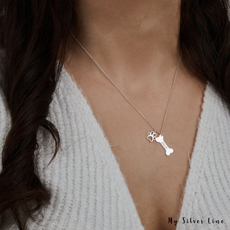 May include: A silver necklace with a bone charm and a paw print charm. The bone charm has the name "Jack" engraved on it.