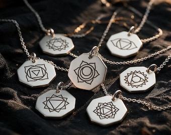 May include: A collection of silver-toned necklaces featuring octagonal pendants. Each pendant is engraved with a distinct geometric chakra symbol in black. The pendants hang from delicate silver-toned chains, showcasing a variety of unique designs.