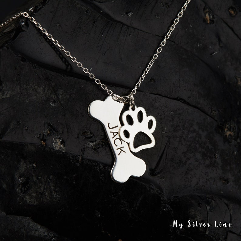 May include: Silver necklace with a bone charm engraved with the name "JACK" and a paw print charm.