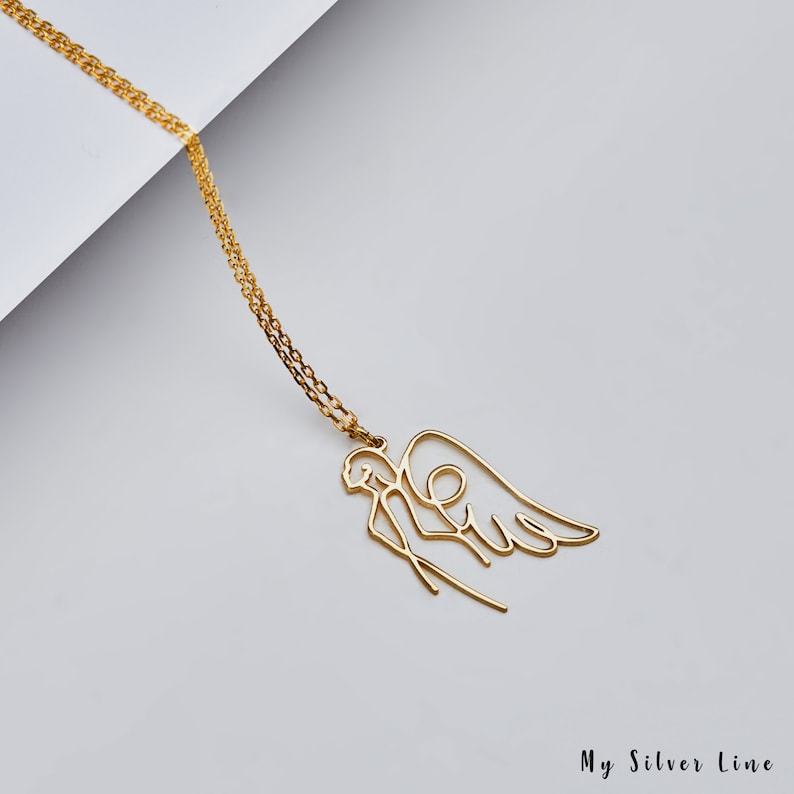 May include: A gold necklace with a delicate angel pendant. The angel is depicted in a single line drawing style with wings outstretched.