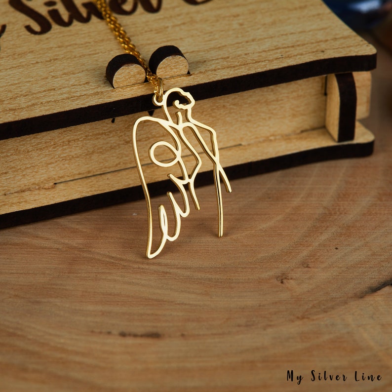 May include: A gold-toned necklace with a delicate angel pendant. The angel is depicted in a simple line drawing style with wings outstretched.
