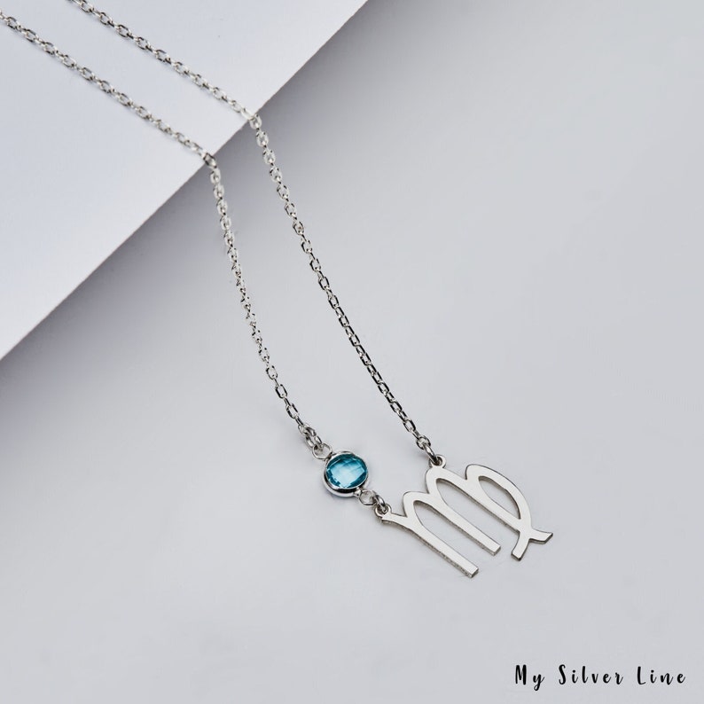 May include: Silver necklace with a blue gemstone and a Virgo zodiac sign pendant.
