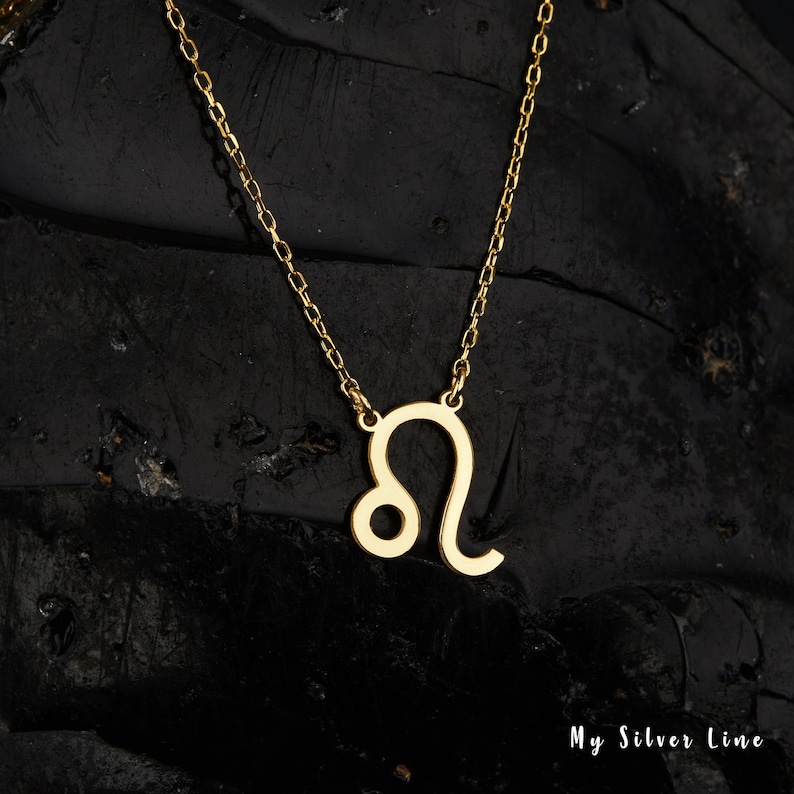 May include: Gold chain necklace with a Leo zodiac sign pendant. The pendant is a simple outline of the Leo constellation.