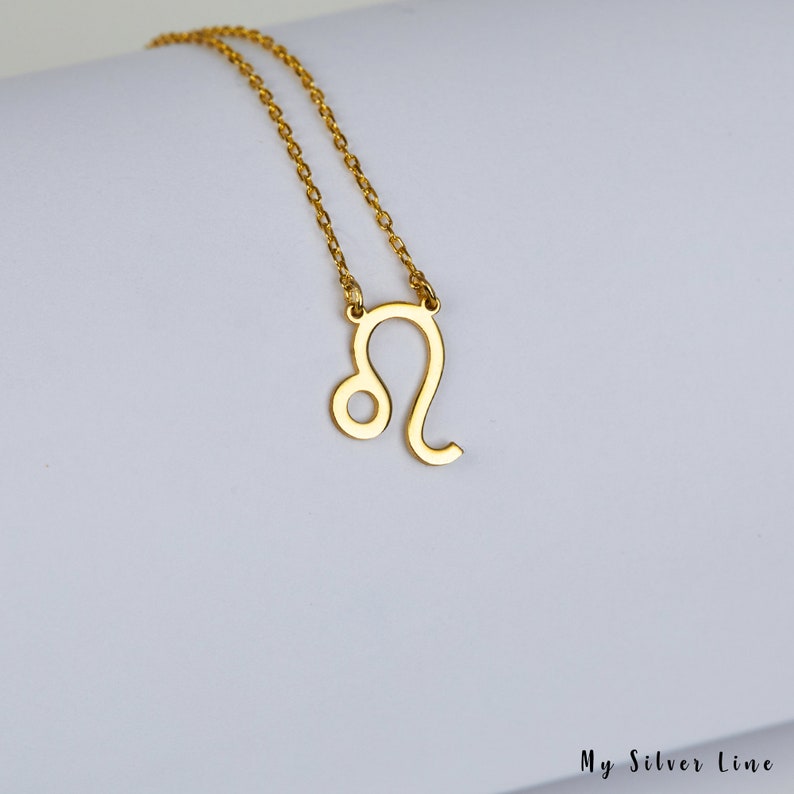 May include: A gold chain necklace with a gold Leo zodiac sign pendant.