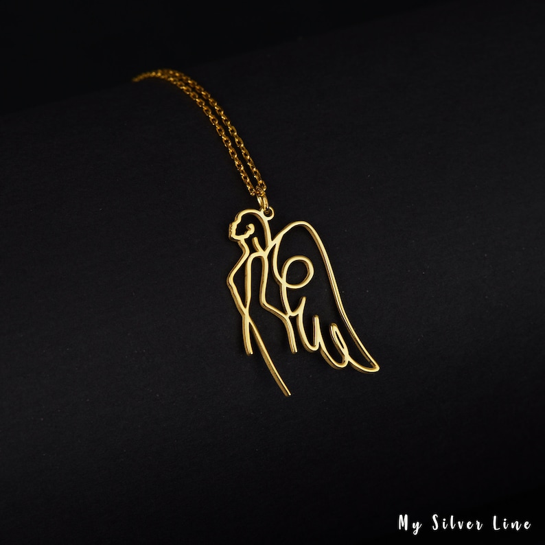 May include: Gold necklace with a delicate, single-line design of an angel with wings. The pendant is a minimalist and modern take on the traditional angel design.
