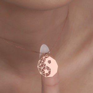May include: A rose gold necklace with a geometric yin yang pendant. The pendant is a delicate, openwork design with a rose gold finish.