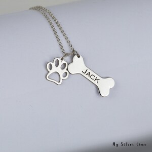 May include: Silver necklace with a bone charm engraved with the name "JACK" and a paw print charm.