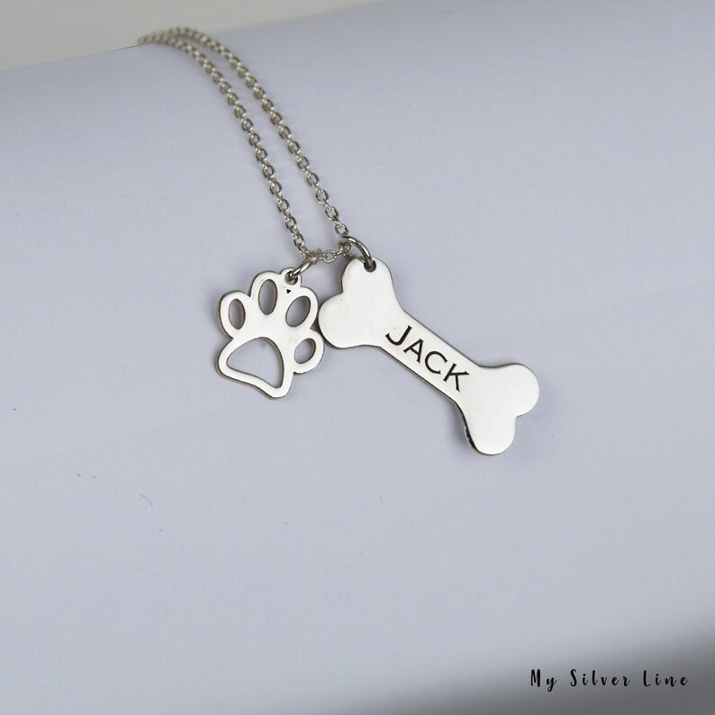 May include: Silver necklace with a bone charm engraved with the name "JACK" and a paw print charm.