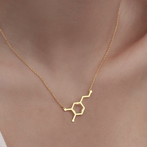 May include: A gold necklace with a pendant shaped like the chemical structure of dopamine.