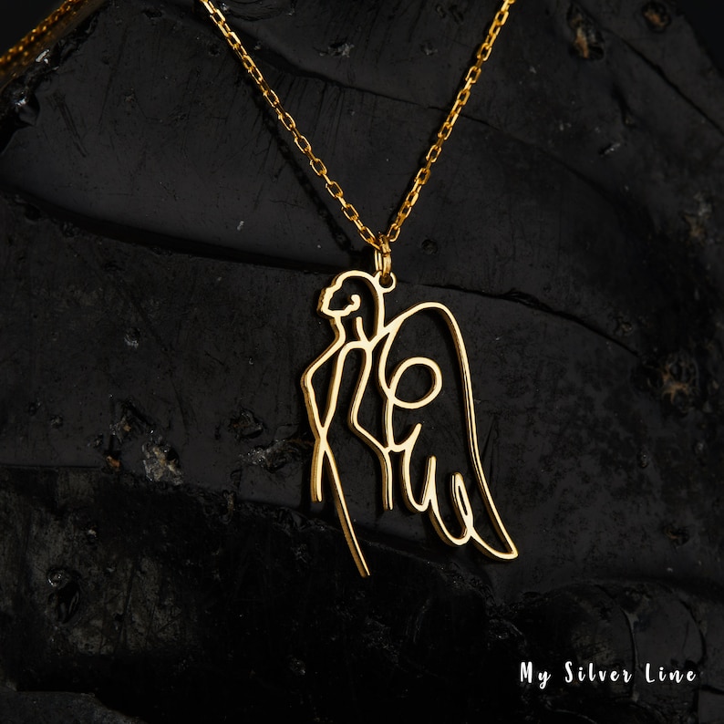 May include: Gold necklace with a delicate angel pendant. The pendant is a single line drawing of an angel with wings.