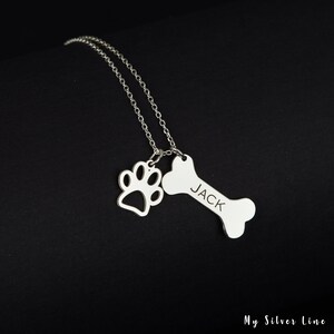 May include: Silver necklace with a bone charm engraved with the name "JACK" and a paw print charm.
