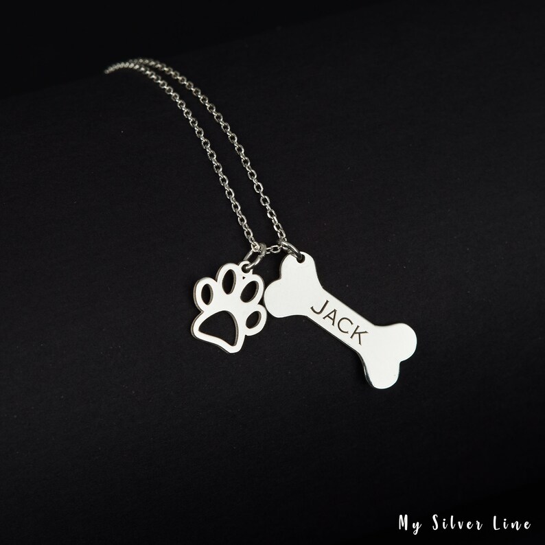 May include: Silver necklace with a bone charm engraved with the name "JACK" and a paw print charm.