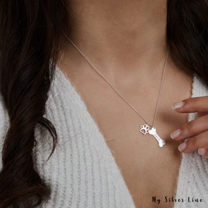 May include: Silver necklace with a bone charm and a paw print charm. The bone charm is engraved with the name "Jack".