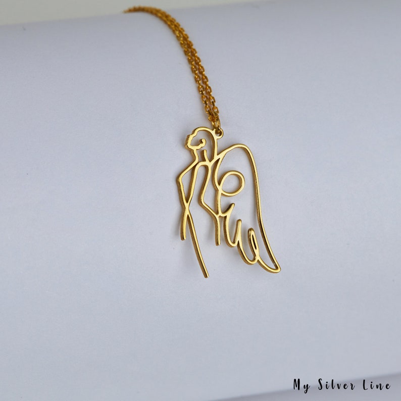 May include: A gold-toned necklace with a delicate, single-line design of an angel with wings. The necklace is on a white background.