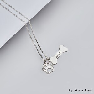 May include: Silver necklace with a bone charm engraved with the name "JACK" and a paw print charm.