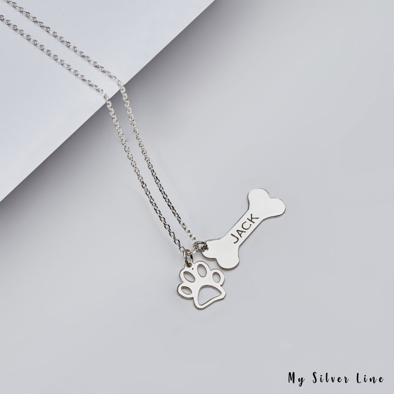 May include: Silver necklace with a bone charm engraved with the name "JACK" and a paw print charm.