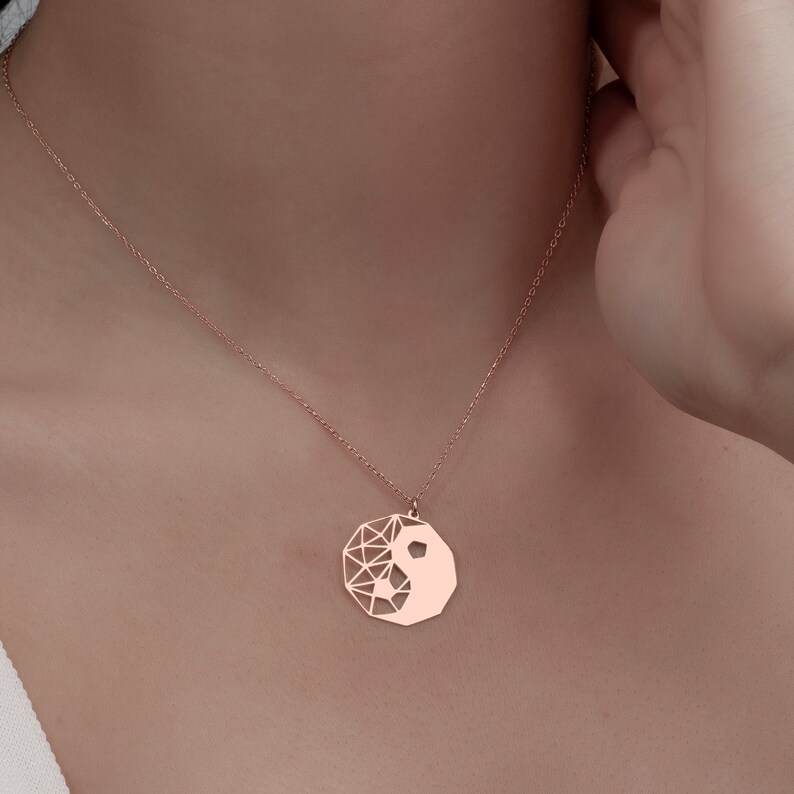 May include: A rose gold necklace with a geometric yin yang pendant.