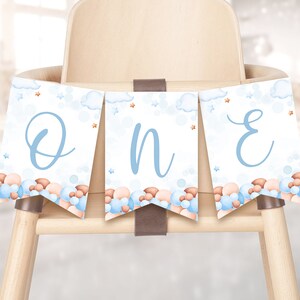 May include: A blue and brown high chair banner with the word "ONE" in blue script. The banner has a cloud and star pattern with blue and brown balloons.