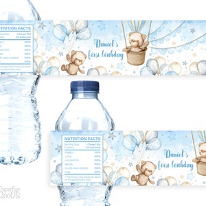 Könnte beinhalten: Wasserflaschenetikett mit einem blauen und weißen Aquarelldesign, das einen Teddybären in einem Heißluftballon zeigt. Das Etikett lautet "Daniel's first birthday".