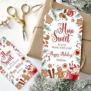 May include: A white gift tag with a red and green watercolor design featuring gingerbread cookies, candy canes, and cinnamon sticks. The text on the tag reads "How Sweet It is to Work with you! Happy Holidays! Melissa".