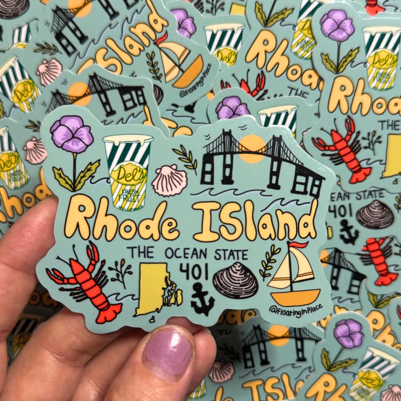 Op de afbeelding: Een lichtblauwe sticker in de vorm van Rhode Island, met illustraties van een brug, zeilboot, kreeft en een Del's frozen lemonade beker. De tekst "Rhode Island" en "The Ocean State" zijn ook opgenomen.