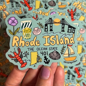 Op de afbeelding: Een kleurrijke sticker met een kaart van Rhode Island, met illustraties van een kreeft, zeilboot, brug en een Del's frozen lemonade beker. De tekst bevat "Rhode Island", "The Ocean State" en "401".