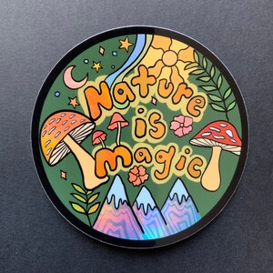 K&ouml;nnte beinhalten: Ein runder Aufkleber mit gr&uuml;nem Hintergrund und dem Text "Nature is magic" in bunten, stilisierten Buchstaben. Der Aufkleber zeigt Pilze, Sterne und eine Sonne mit Strahlen.