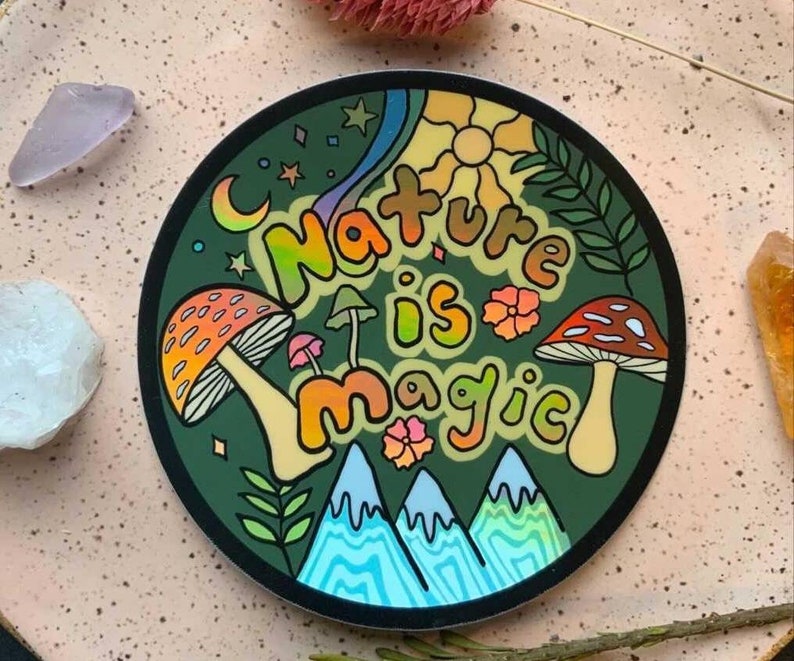 K&ouml;nnte beinhalten: Ein runder Aufkleber mit gr&uuml;nem Hintergrund und dem Text "Nature is magic" in Regenbogenfarben. Der Aufkleber zeigt Pilze, Berge, Sterne und eine Sonne.