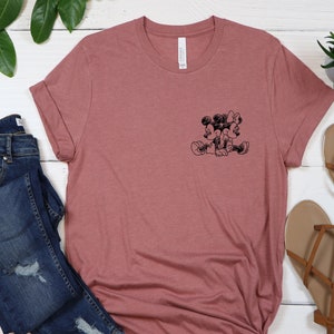 May include: A mauve t-shirt with a black and white image of Mickey Mouse and Minnie Mouse on the front.