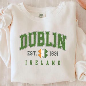 Peut inclure: Sweat-shirt blanc avec un tr&egrave;fle graphique vert, blanc et orange et le texte "Dublin Est. 1631 Irlande".