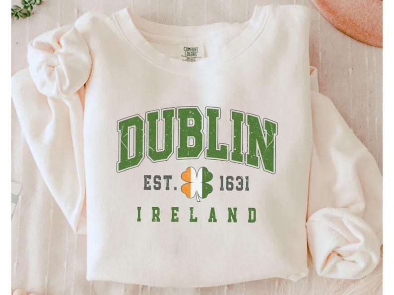 Peut inclure: Sweat-shirt blanc avec un tr&egrave;fle graphique vert, blanc et orange et le texte "Dublin Est. 1631 Irlande".