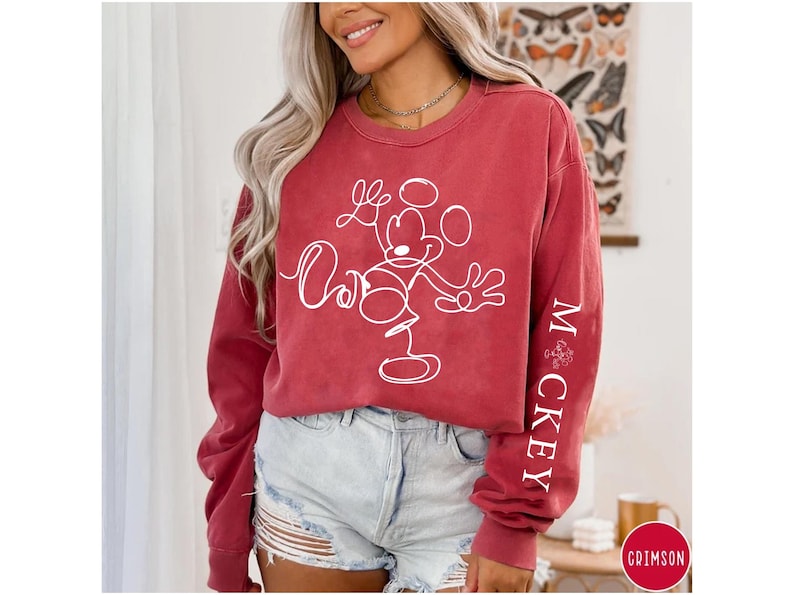 Puede incluir: Una sudadera roja de manga larga con un contorno blanco de Mickey Mouse y el texto "Mickey" en la manga.