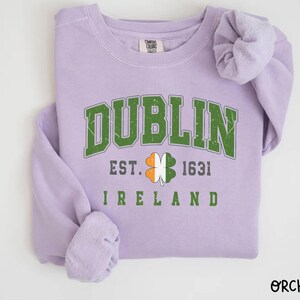 Peut inclure: Un sweat-shirt lavande avec le texte "DUBLIN EST. 1631 IRLANDE" et un tr&egrave;fle vert avec des accents orange et blanc.