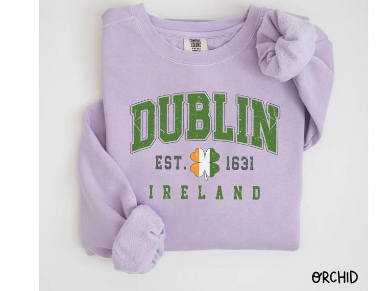 Peut inclure: Un sweat-shirt lavande avec le texte "DUBLIN EST. 1631 IRLANDE" et un tr&egrave;fle vert avec des accents orange et blanc.